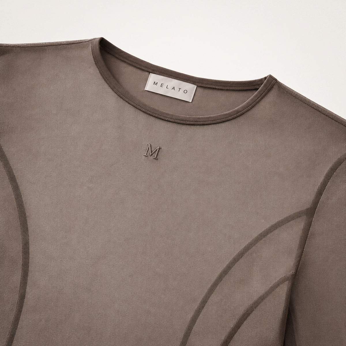 Close-up of the Melato Body Language Cocoa Mesh Bodysuit showing sheer cocoa mesh, contour seamwork, crew neckline, and tonal Melato label.