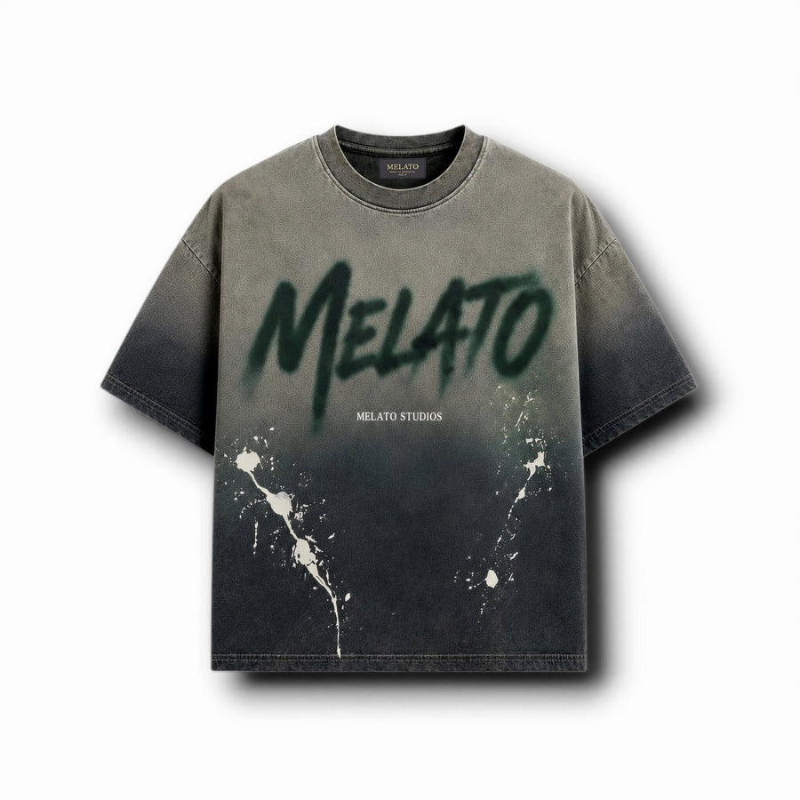 A short-sleeve crewneck t-shirt with a dark gray to black gradient wash, featuring a large green spray-paint style 'MELATO' graphic on the chest, smaller 'MELATO STUDIOS' text, and white paint splatters near the lower front.